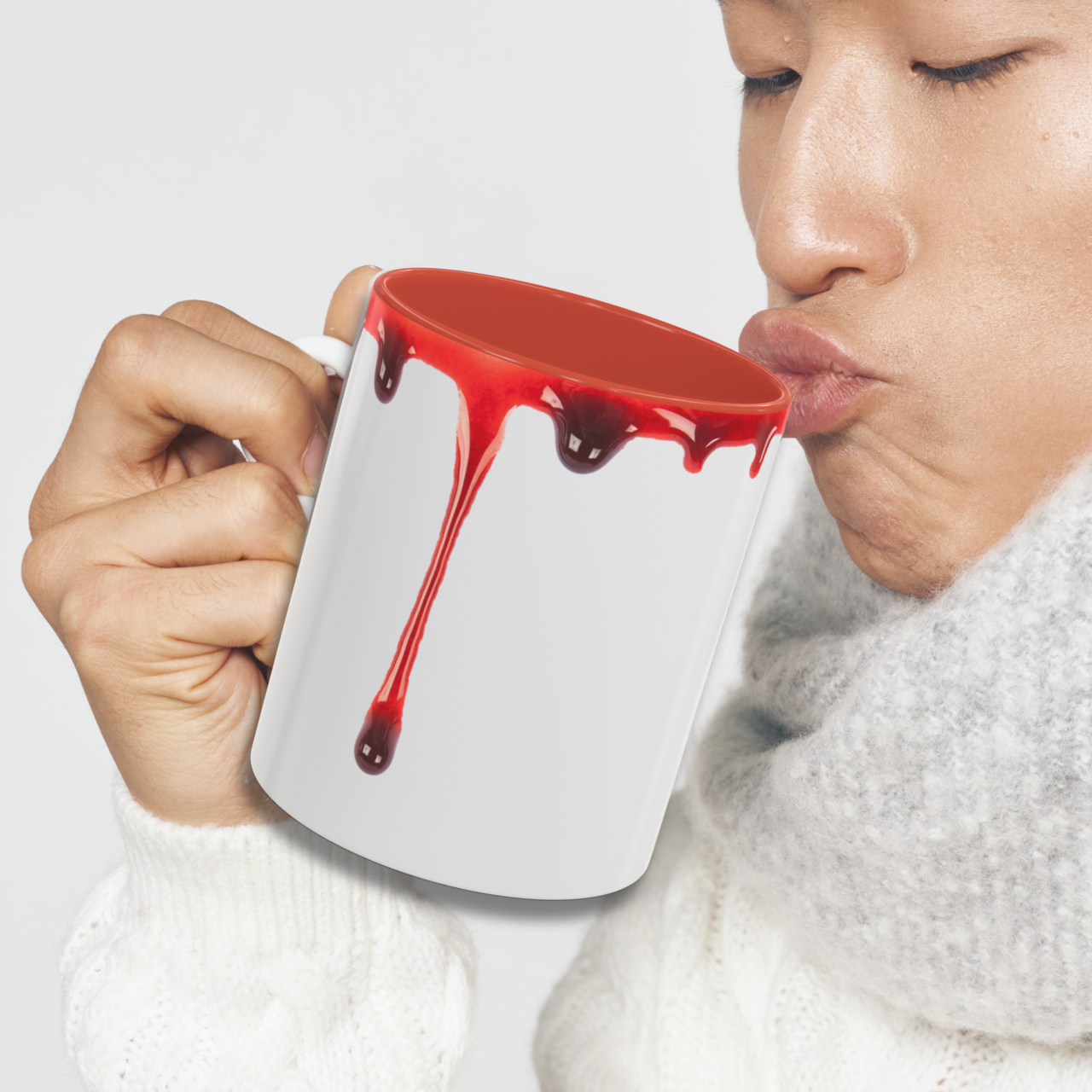 Person drinking from a mug with red blood dripping, on a plain background
