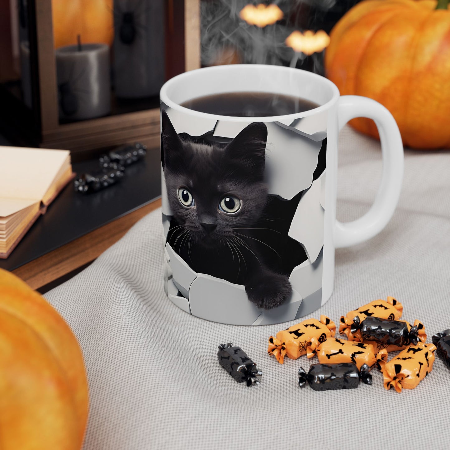 Mug with a black cat design on a table with Halloween-themed treats and pumpkins.