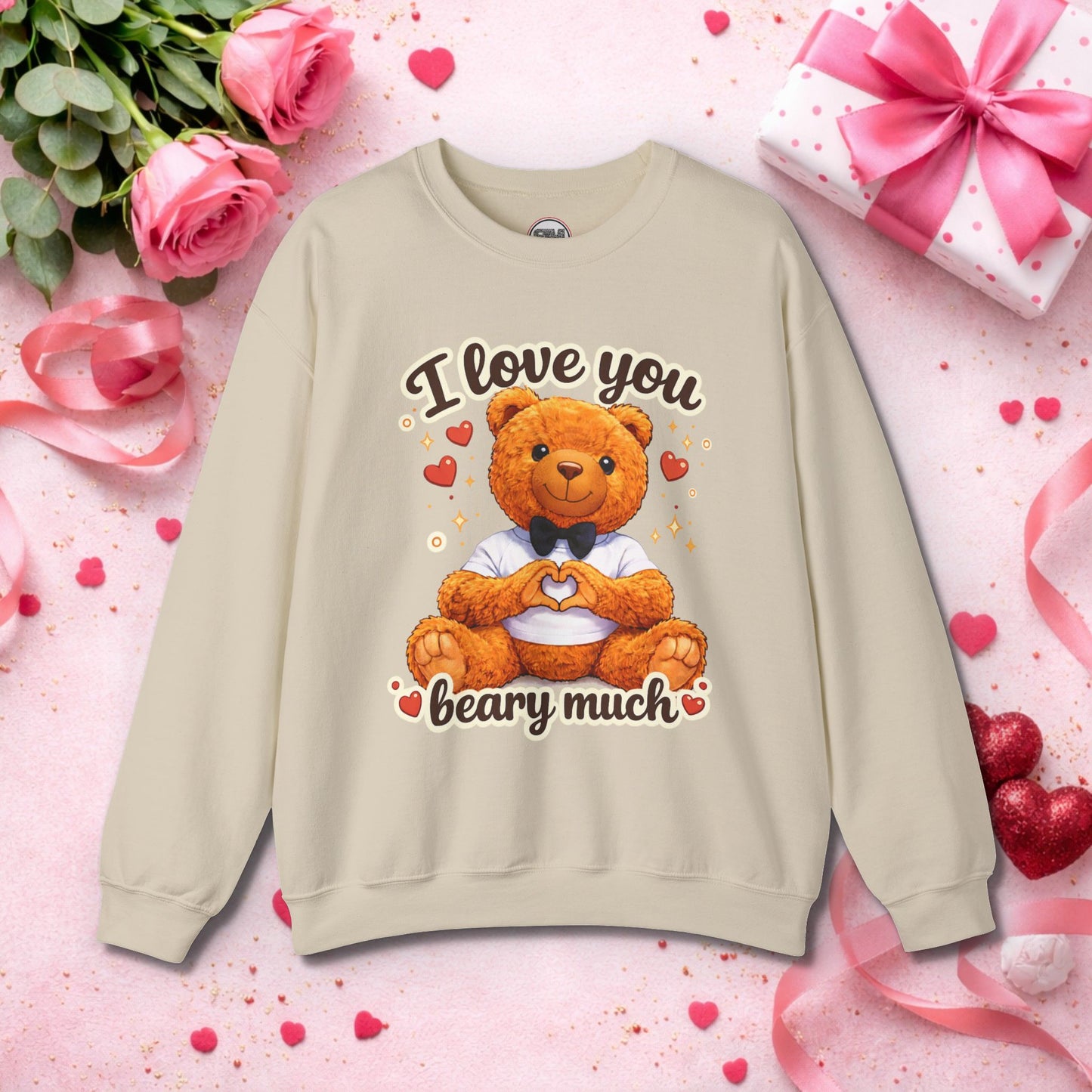 Cute brown teddy bear sitting on a cozy white sweatshirt, forming a heart shape with its paws, wearing a black bow tie and white shirt, surrounded by red hearts and sparkles with "I Love You Beary Much" pun text – perfect Valentine's Day gift sweatshirt for her