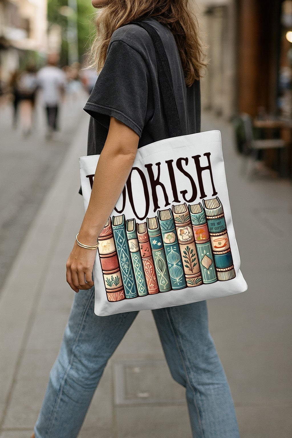Person holding a tote bag with book design and 'BOOKISH' text on a city street.